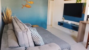 Ein modernes Wohnzimmer mit einem grauen Sofa, einem flachbildfernseher an der Wand und einem kleinen Holztisch.