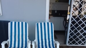 Zwei weiße Lounge-Sessel mit blau-weißen Kissen auf einer Holzterrasse.