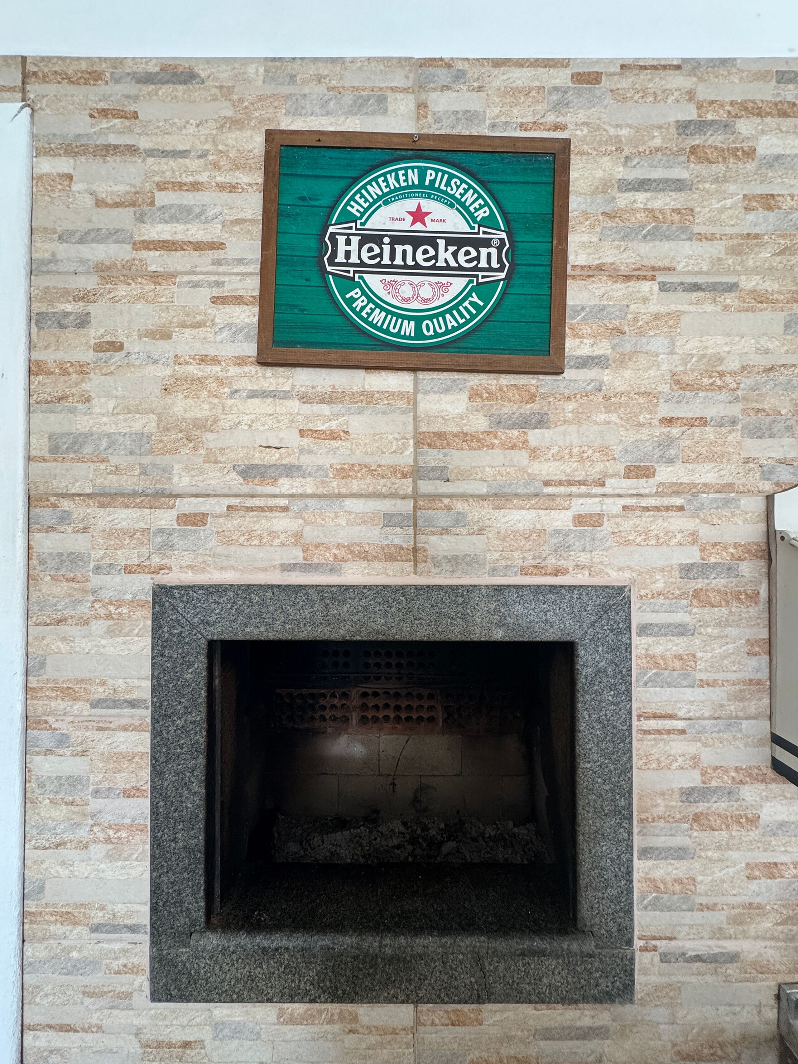 A Heineken sign mounted on a stone wall above a fireplace.