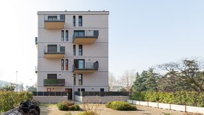 Um edifício residencial com vários andares, varandas, entrada com portão e um pátio ajardinado.
