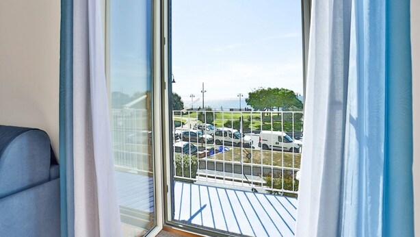 Ein Zimmer mit Schiebetür zum Balkon, ein blauer Stuhl und Blick auf geparkte Autos und Grünflächen.