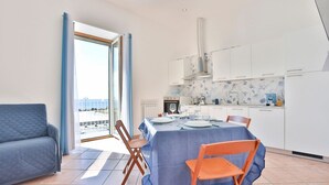 Eine moderne Küche mit Esstisch für vier Personen, einer Couch und Meerblick durch ein großes Fenster.