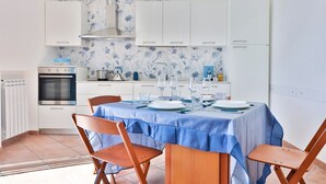 Eine moderne Küche mit weißen Schränken, einer blauen Rückwand mit Blumenmuster und einem Esstisch für vier Personen.