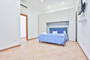 A bedroom with a bed, a desk, and a TV mounted on the wall. - GuestHost - Charming 60 sqm apartment, ideal for up to 3 people, located on the first floor of a building without an elevator.The property is located in Pozzuoli, in a strategic position that allows easy access to the city center and the metro and train  (Pozzuoli)