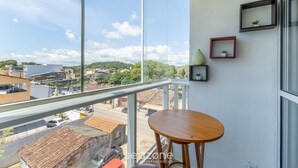 A balcony with a wooden table, a glass railing, and framed pictures on the wall. - Apt w/ Balcony Near the Beach in Ilheus Rpd0301 (Ilhéus)
