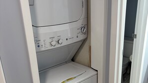 A compact washer and dryer unit with control panel, located in a small laundry room with a wooden floor and a door leading to a bathroom. - 2BR 1B condo Amelia island, 2 blocks beach 2 miles downtown 1 mile Fort Clinch (Fernandina Beach)