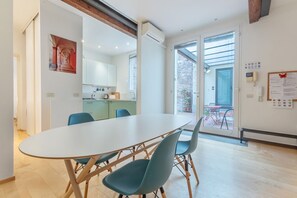 Ein moderner Essbereich mit einem großen Tisch und Stühlen, eine Küche im Hintergrund und eine Glastür, die zu einem Außenbereich führt.