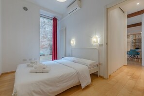 Ein modernes Schlafzimmer mit einem Bett, einem Fenster mit roten Vorhängen und Blick auf eine Ziegelwand.