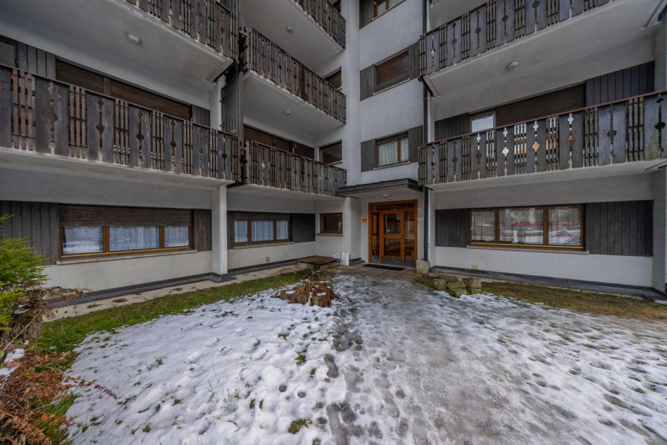 A multi-story building with balconies, a central courtyard, and a snow-covered ground.