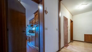 A hallway with a wooden door leading to a kitchen with cabinets and a stove. - GuestHost - In Tarvisio, a cozy 35 sqm studio for 2 guests, located on the second floor of a residential building with an elevator (not suitable for disabled persons). Surrounded by greenery, the building offers an open view of the city center, the sport (Tarvisio)