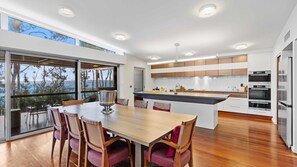 A modern kitchen with a central island, built-in ovens, and a dining area with a view. - The Villa at Maloneys (Maloneys Beach)
