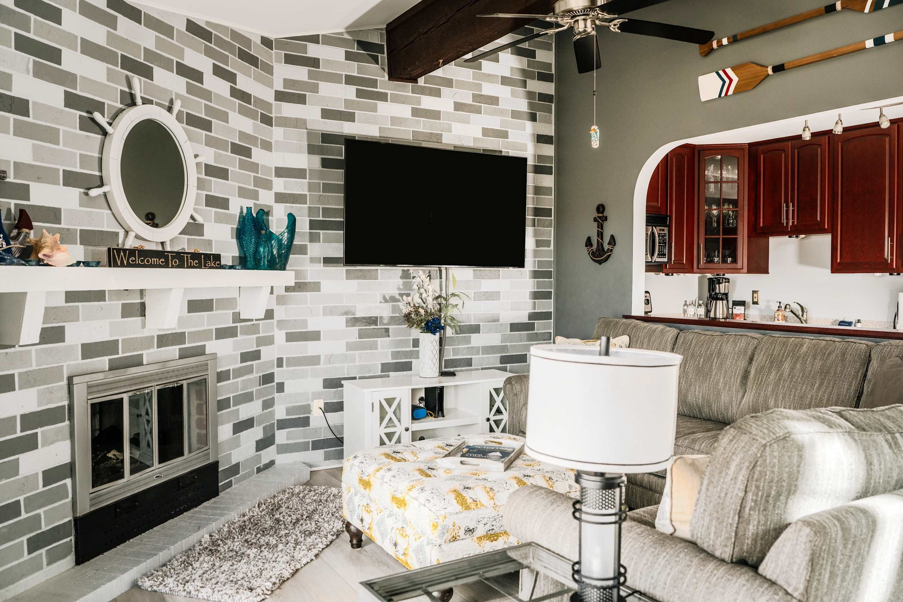 A living room with a fireplace, a television, a sofa, and a kitchen area with wooden cabinets.