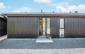 Ein modernes Gebäude mit dunkler Fassade, einem Glastür-Eingang und einer Auffahrt mit Kies.
