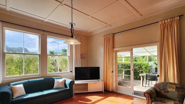 Un soggiorno con divano, televisione e vista su un giardino attraverso ampie finestre.