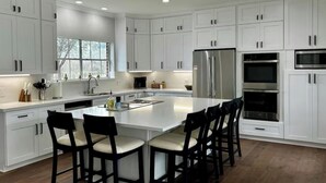 A modern kitchen with white cabinets, a central island with chairs, stainless steel appliances, and a window providing natural light. - Beautiful Private 30 Acre Nature Retreat/Pool
Ideal for family/groups sleeps 16 (Plantersville)