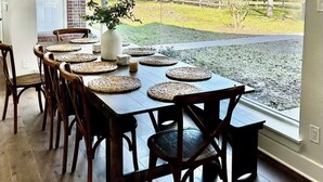 A dining area with a large table set for six, wooden chairs, a hanging light fixture, and a view of a grassy yard through large windows. - Beautiful Private 30 Acre Nature Retreat/Pool
Ideal for family/groups sleeps 16 (Plantersville)