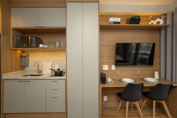 A modern kitchen with a built-in microwave, sink, and a dining area with a TV and two chairs. - For You Perdizes (São Paulo)