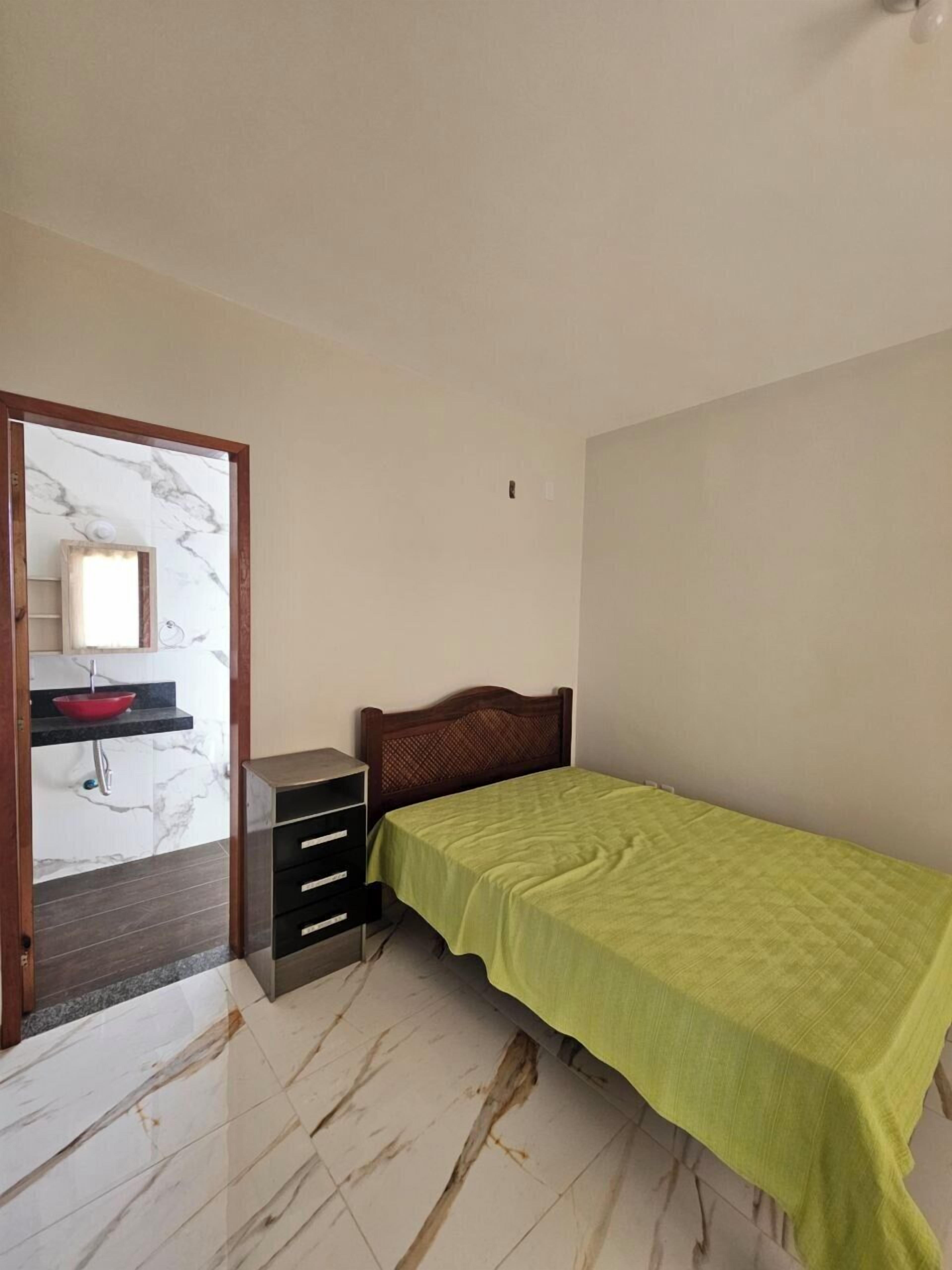 Un dormitorio con cama, mesita de noche, cómoda y baño con lavabo y espejo.