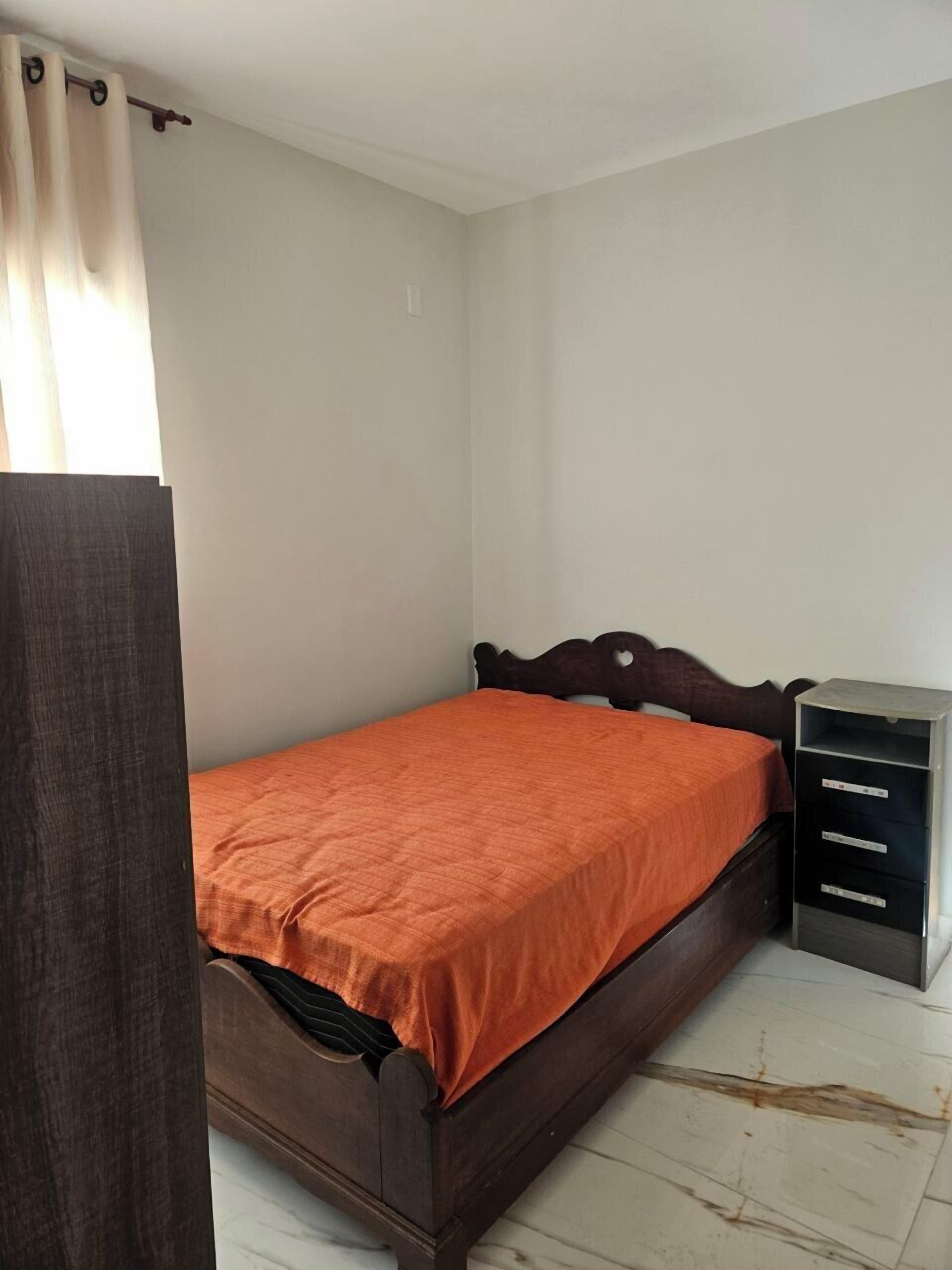 Ein Einzelbett mit orangefarbener Bettdecke in einem Zimmer mit weißen Wänden und einem hölzernen Kopfteil.