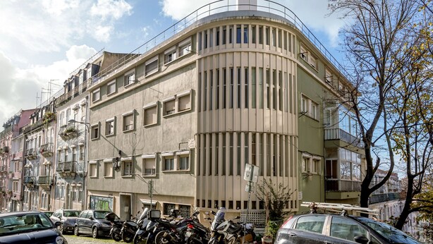 A multi-story building with a curved facade, balconies, and a parking area with cars and motorcycles. - Anjos City Center Apartment by Homing (Lisbon)