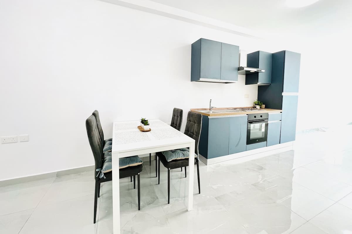 A compact kitchen with a white table and chairs, a small island with a sink, and blue cabinets.