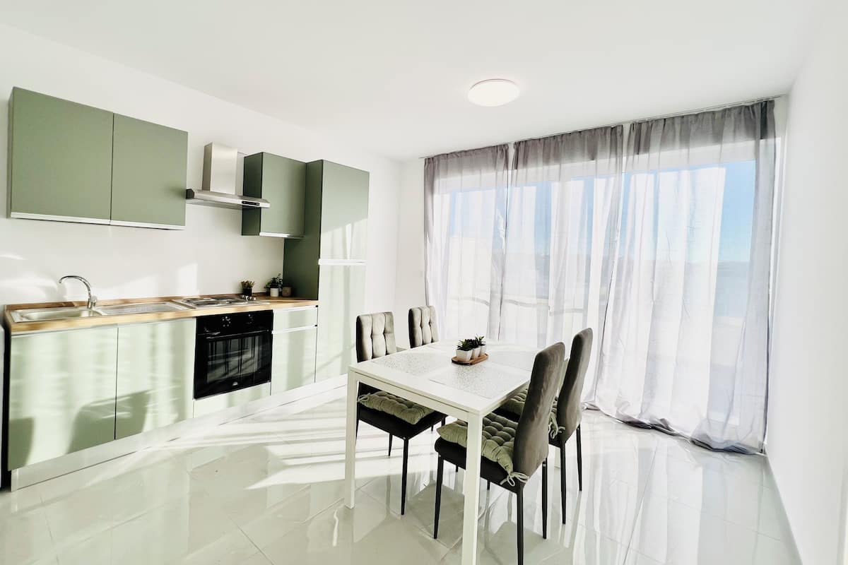 A modern kitchen with a dining area, large windows, and a view of the outdoors.