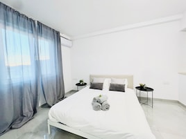 Camera d'albergo moderna con un letto grande, due comodini, una piccola pianta in vaso e una finestra con tende.