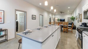 A modern kitchen with a central island, wooden chairs, a dining table, and a TV. - Tucson Summer Base | 4BR Modern Duplex Retreat (Tucson)
