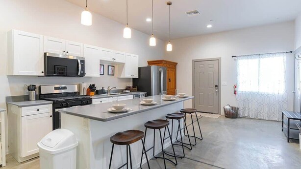 A modern kitchen with white cabinets, a central island with stools, stainless steel appliances, and pendant lighting. - Tucson Summer Base | 4BR Modern Duplex Retreat (Tucson)