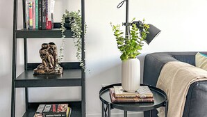 En moderne stue med en sort bogreol, en gulvlampe, et rundt bord med en plante og en sofa.
