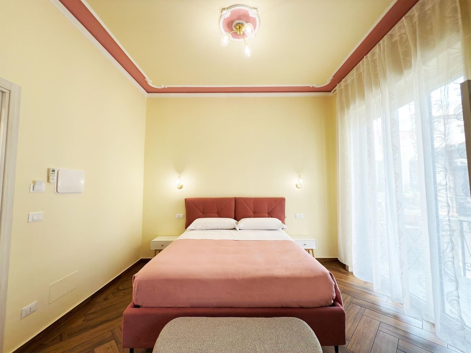 A bedroom with a bed, bedside tables, a ceiling light, and a window with curtains.