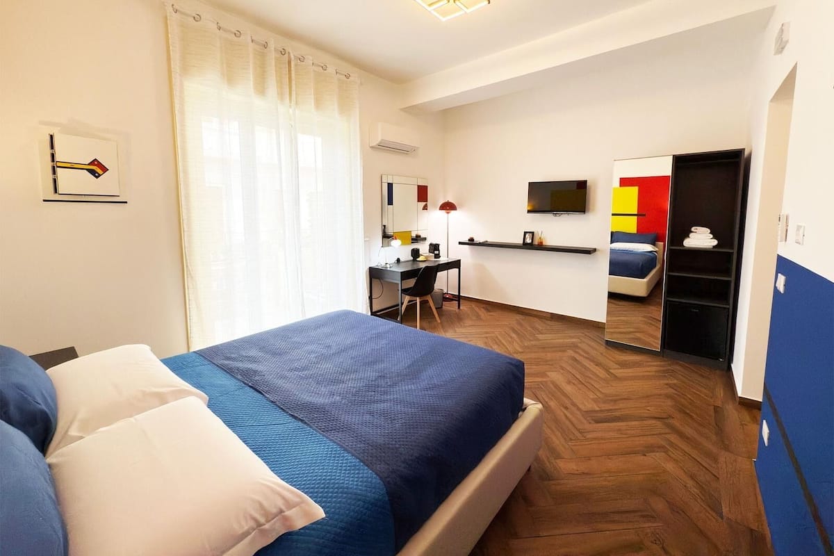 A hotel room with a bed, a desk, a chair, a TV, and a wardrobe.