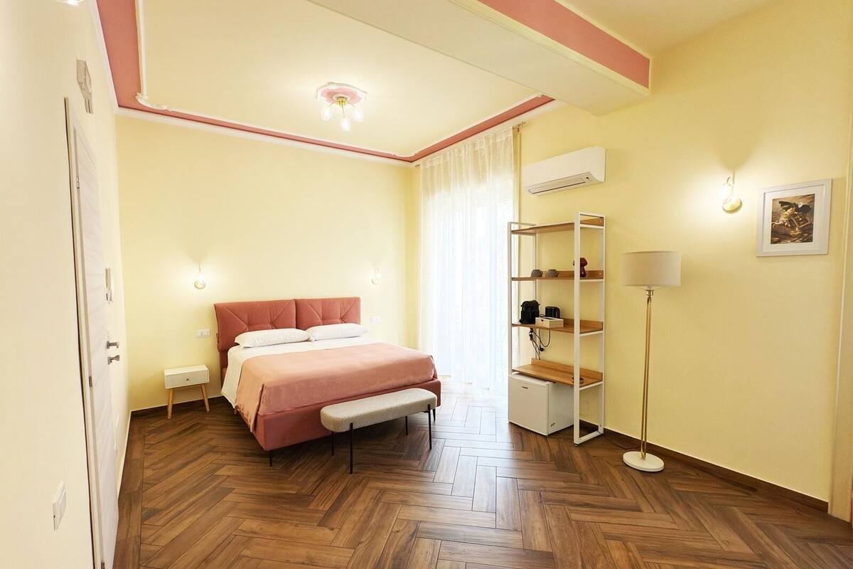 A bedroom with a bed, bench, bedside table, wardrobe, and a floor lamp.