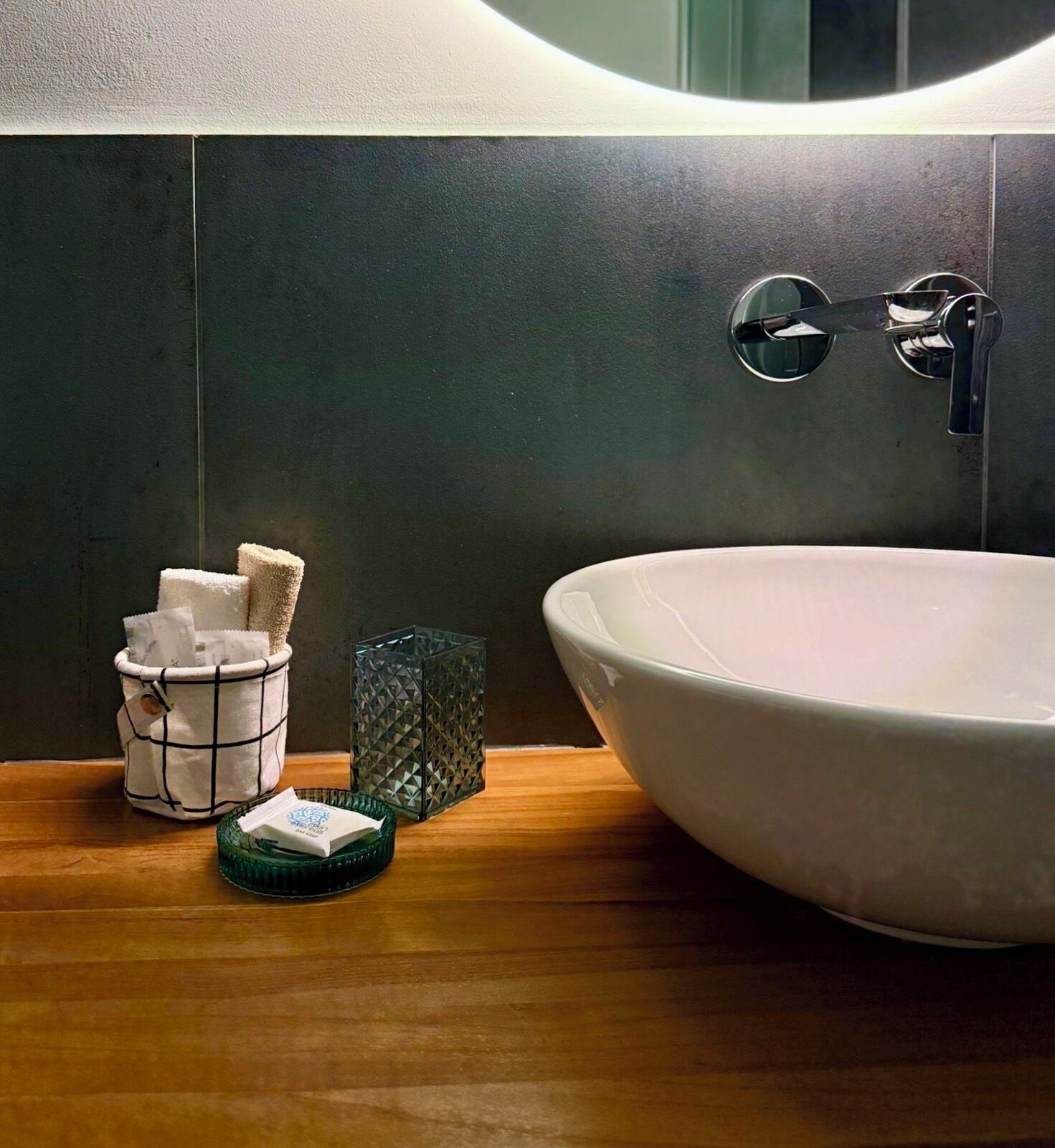 A bathroom with a large white sink, a towel holder with folded towels, a glass container, and a wooden countertop.