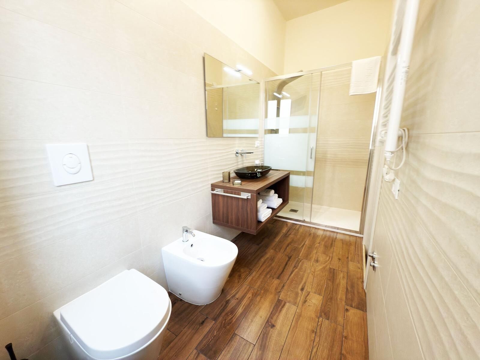 Une salle de bain moderne équipée de toilettes, d’un bidet, d’un meuble-lavabo en bois et d’une douche à parois de verre.