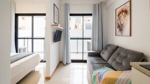 Una sala de estar moderna con un sofá gris, un televisor de pantalla plana montado en la pared y un ventanal con cortinas.