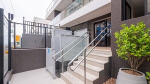 Un edificio moderno con una escalera que conduce a una entrada protegida por un muro, una planta en maceta y vistas despejadas del entorno.