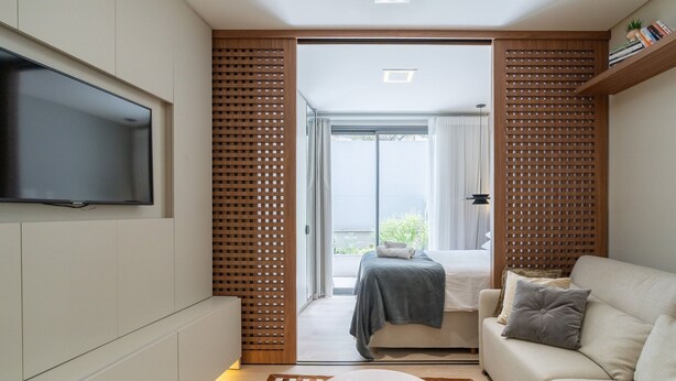 A modern hotel room with a flat-screen TV mounted on the wall, a sofa, a bed with a gray blanket, and a checkered rug. - Studio 300m From Beira-mar Norte Msg0101 (Florianópolis)