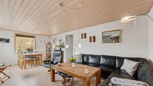 A spacious living room with a wooden ceiling, a black leather sofa, a wooden dining table with chairs, and a large window. - Nice home in Thyborøn with WiFi (Thyborøn)