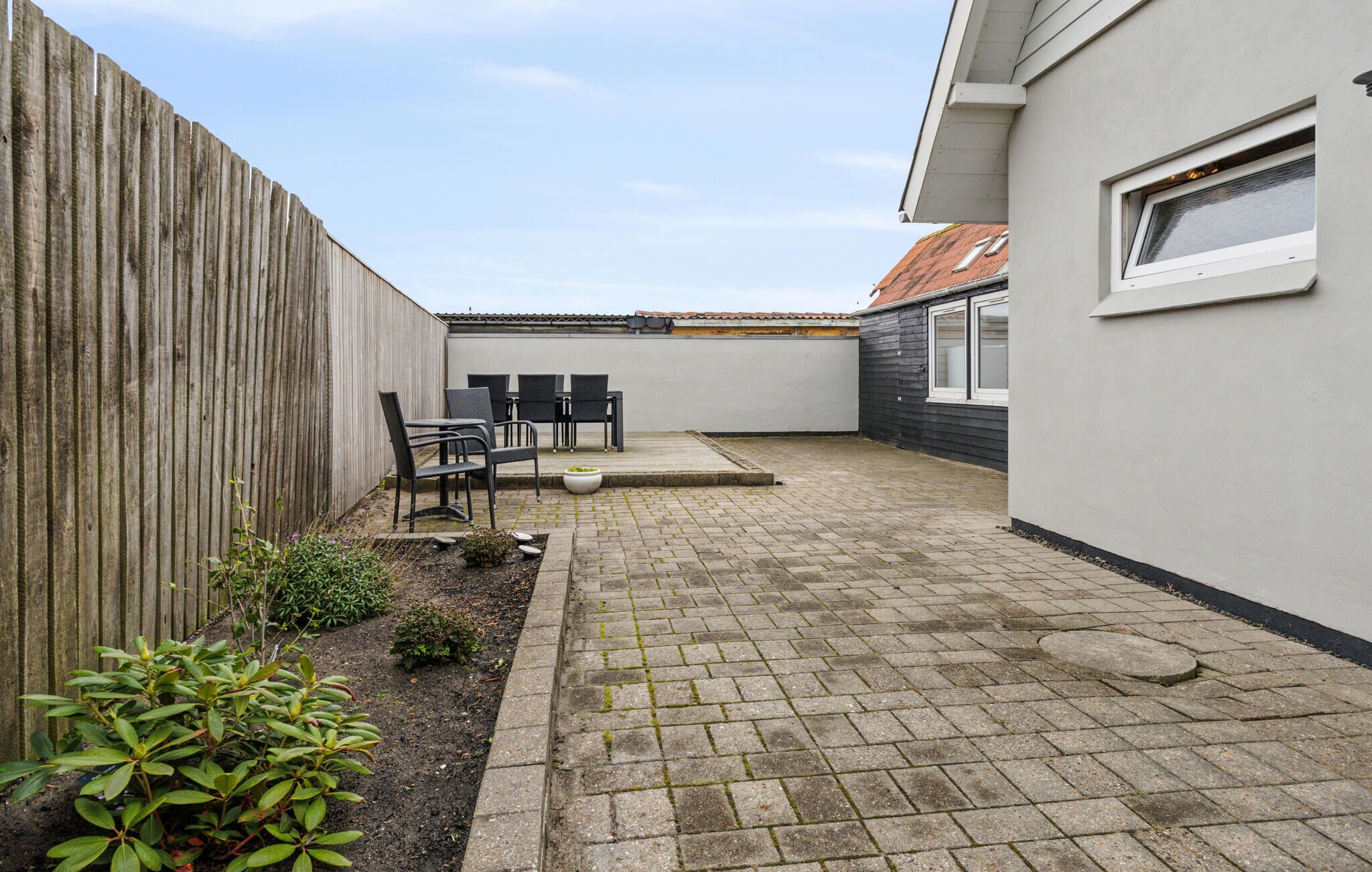 A patio area with a table and chairs, a wooden fence, and a small garden.
