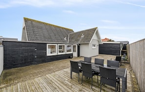 A patio area with a wooden deck, a table with chairs, and a small building with windows. - Nice home in Thyborøn with WiFi (Thyborøn)
