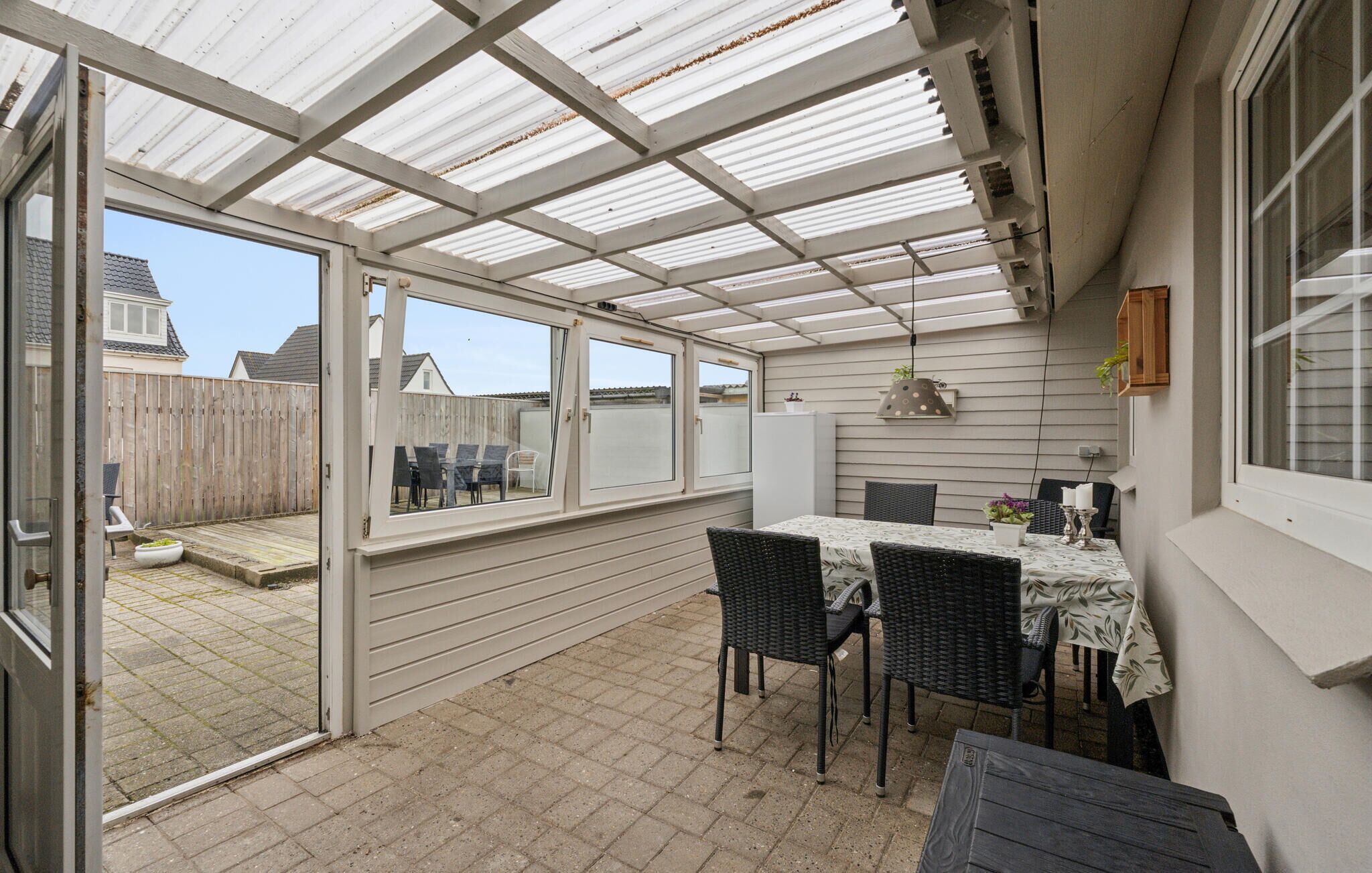 A covered patio with a table and chairs, a wooden fence, and a view of a residential area.