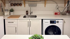 Een keuken met witte kasten, een wasmachine, een magnetron en diverse keukenattributen en apparaten.