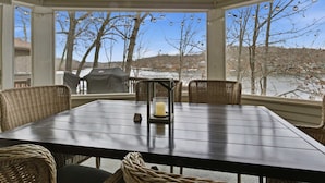 Un patio cubierto con una mesa y sillas, un centro de mesa con velas y vistas a árboles y un cuerpo de agua.