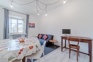 Una stanza con un tavolo da pranzo, una poltrona, una TV e una finestra con tende.