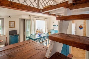 Ein Holzespeisetisch mit Stühlen, ein Fernseher auf einem Schrank und Blick auf einen Raum mit einem blauen Schrank und einem Fenster.