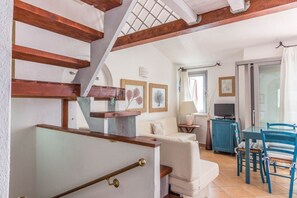 Eine Treppe mit Holzbalken, ein weißes, gepolstertes Sofa, ein kleiner Tisch mit einer Lampe und ein Fernseher auf einem Schrank.