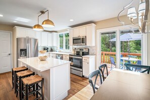 A modern kitchen with white cabinets, stainless steel appliances, and a large island with stools. - The Retreat at Afton Mountain (Afton)