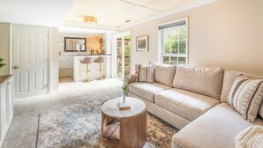 Ein geräumiges Wohnzimmer mit einem beigen Sofa, einem runden Couchtisch und einem gemusterten Teppich.