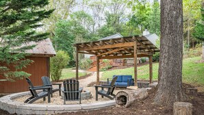 Eine Holzterrasse mit Adirondack-Stühlen und einem Feuerkorb, umgeben von einem Steinrand und einer Holzpergola.